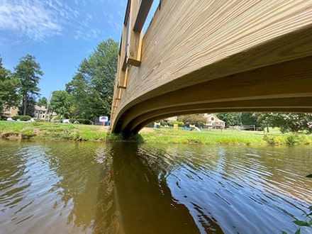 Photo showing curved wooden arch bridge over a small creek.